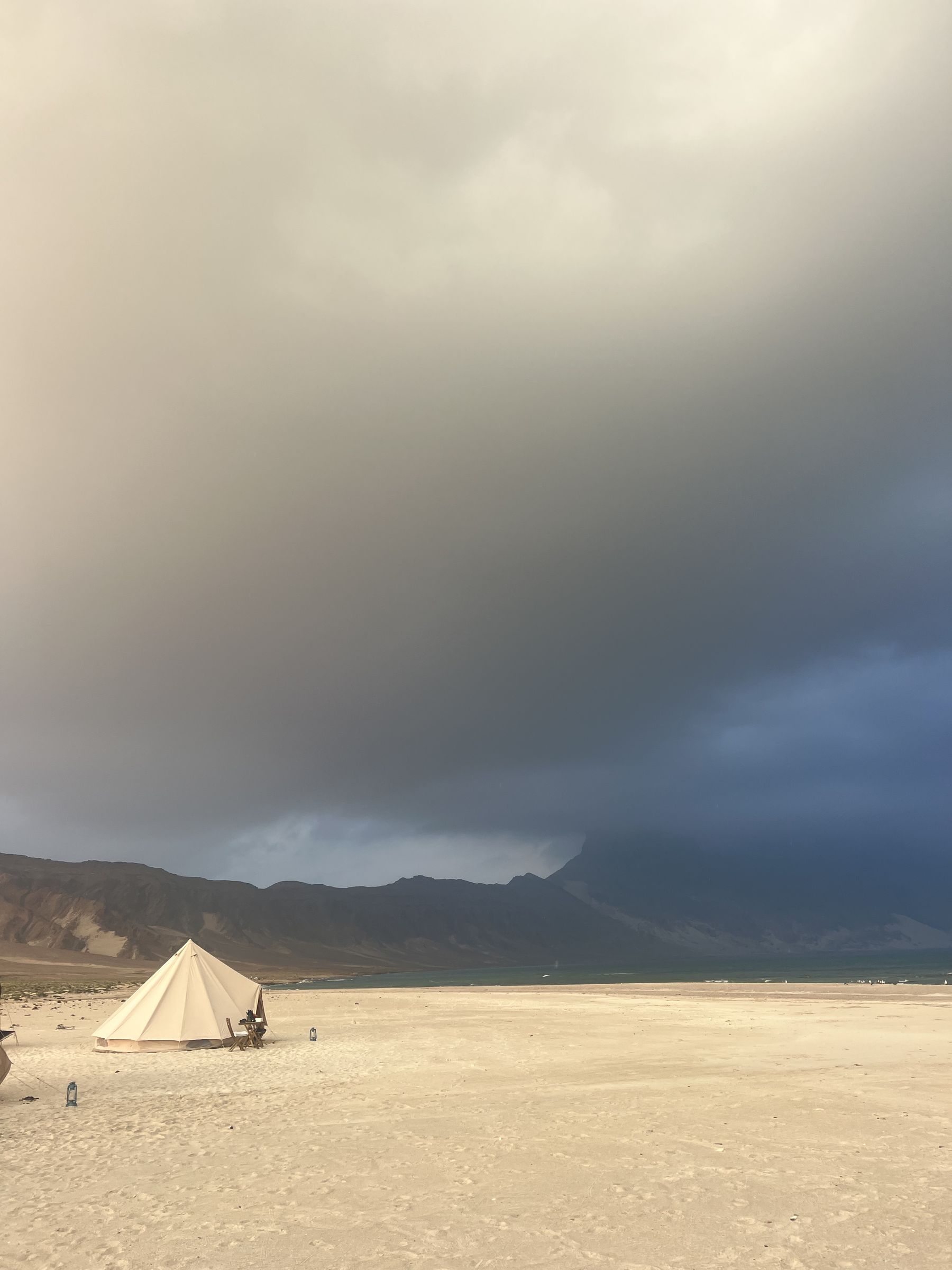 A bell tent on a white beach on Socotra under a heavy storm cloud